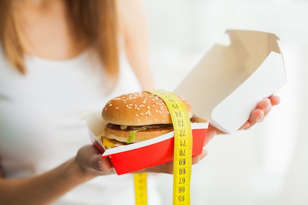 Foto een jonge vrouw die een hamburger in een meetlint houdt.