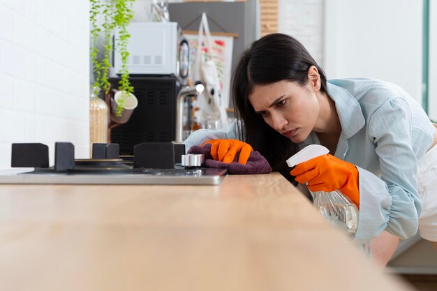 Een jonge vrouw die een keukentafel met een spuitfles schoonmaakt De vrouw draagt een schort en handschoenen