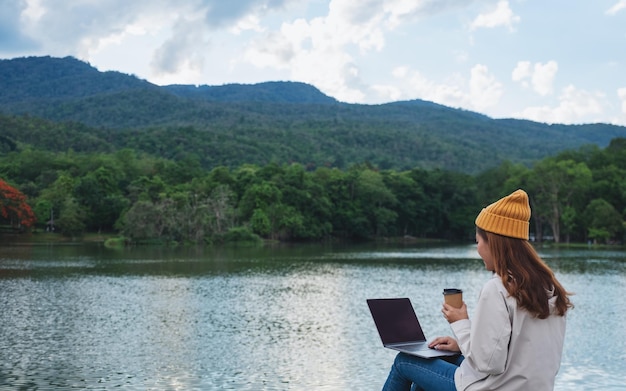 Een jonge vrouw die een laptop gebruikt en erop werkt terwijl ze door bergen en meren reist