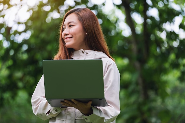 Een jonge vrouw die een laptop in de buitenlucht vasthoudt en gebruikt