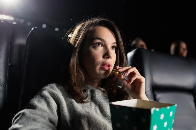 Een jonge vrouw die gepassioneerd is door een blockbuster eet popcorn in de bioscoop Moderne bioscoopzaal met lederen fauteuils
