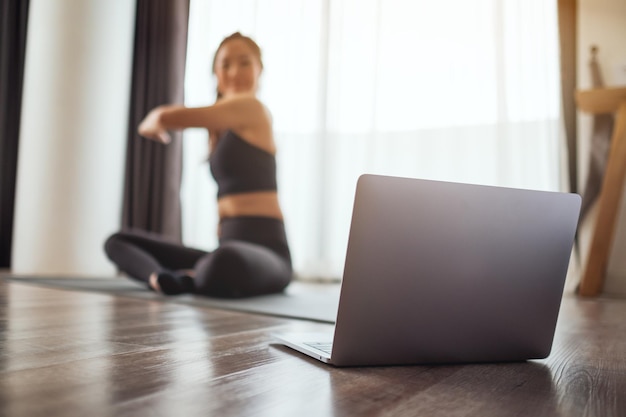 Een jonge vrouw die haar armen uitstrekt terwijl ze thuis online workout-tutorials op een laptop bekijkt