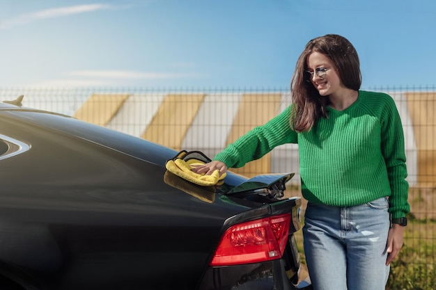 Een jonge vrouw die haar auto schoonmaakt en polijst met een microvezeldoekconcept van autoverzorging