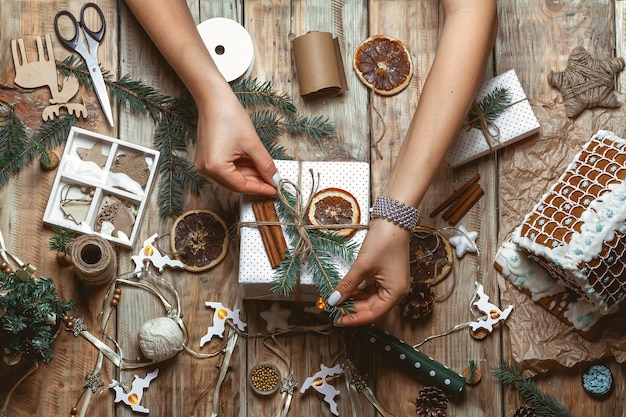 Foto een jonge vrouw die het kerstcadeau op tafel inpakt en decoreert met nieuwjaarsversieringen