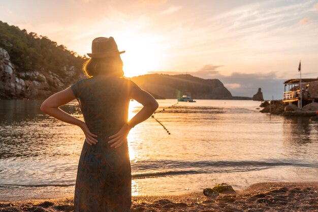 Een jonge vrouw die naar het strand van Benirras in het concept van de zonsondergangvakantie van Ibiza kijkt