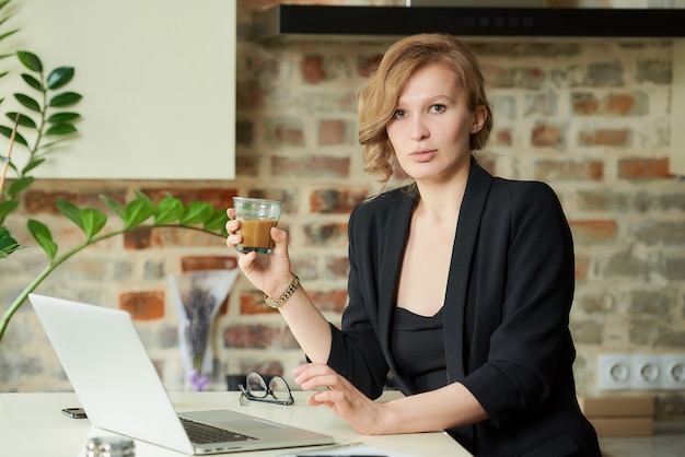 Een jonge vrouw die op afstand in haar keuken werkt. een vrouwelijke baas die koffie drinkt voor een videoconferentie met haar werknemers thuis.