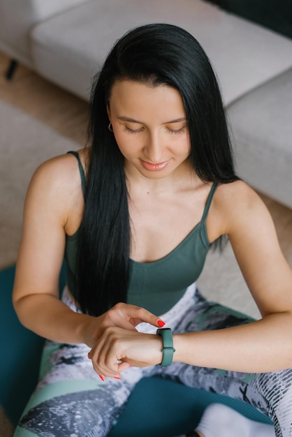 Een jonge vrouw die op de grond zit en naar haar smartwatch kijkt in een gezellig huis