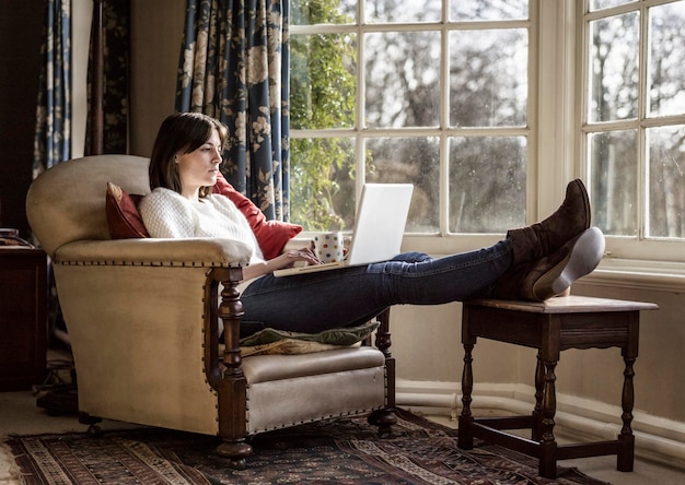 Een jonge vrouw die thuis ontspant met haar voeten omhoog met behulp van een laptop