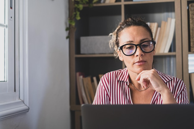 Een jonge vrouw die thuis op kantoor werkt met laptop en notebook die aantekeningen maakt tijdens een videoconferentie Een zakenvrouw die communicatie beltxA