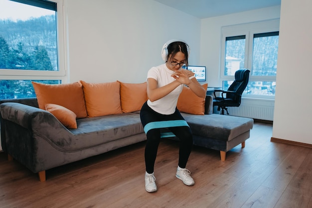 Een jonge vrouw doet squats in een modern appartement met een koptelefoon op haar hoofd om aan te geven dat ze lijst heeft