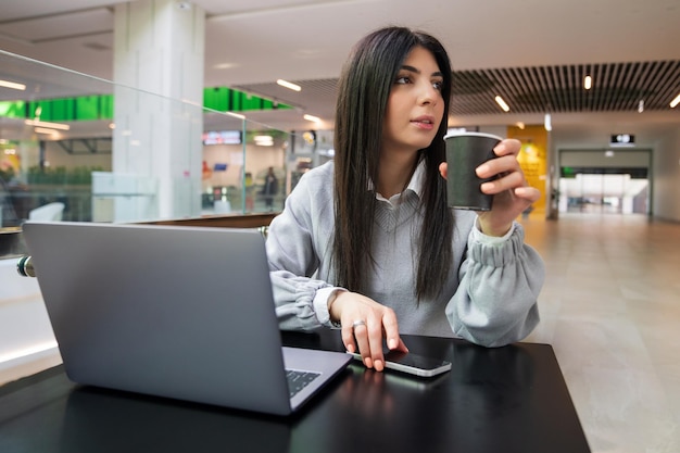Een jonge vrouw drinkt koffie terwijl ze op een laptop in een café werkt