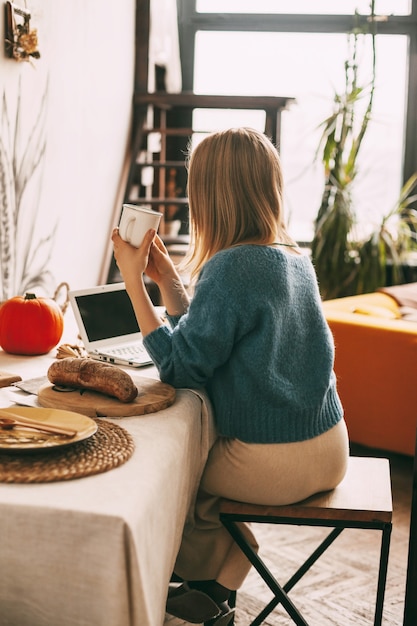 Een jonge vrouw drinkt 's ochtends koffie en werkt op haar laptop