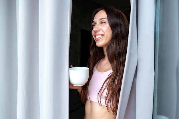 Een jonge vrouw drinkt 's ochtends koffie Glimlachend model op het balkon Zomerochtend