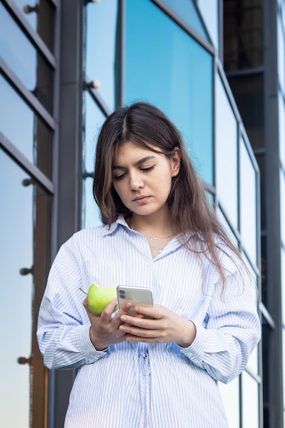 Een jonge vrouw eet een appel met een smartphone in haar handen