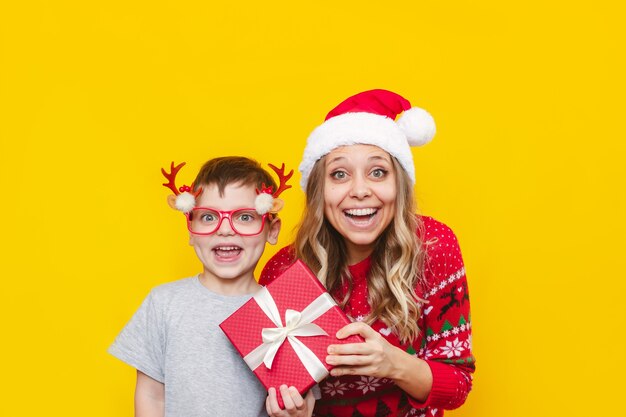 Een jonge vrouw en een klein kind met kerstaccessoires houden de geschenkdoos op een gele achtergrond