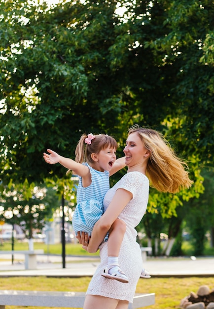 Een jonge vrouw en haar dochter draaien in hun armen. Moeder en dochter lachen en hebben plezier. Moederliefde en tederheid. Familie zomerwandeling in het park.