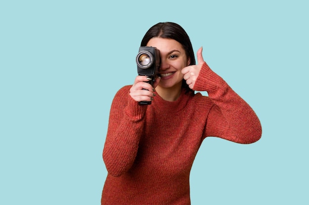 Een jonge vrouw filmt vrolijk met een antieke videocamera op een geïsoleerde achtergrond