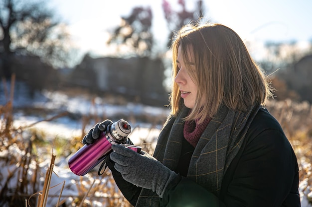 Een jonge vrouw geniet van een warme drank uit een thermoskan tijdens een wandeling in de winter