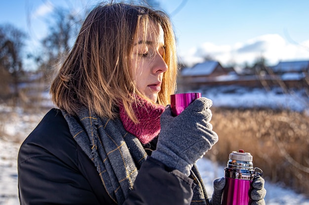 Een jonge vrouw geniet van een warme drank uit een thermoskan tijdens een wandeling in de winter