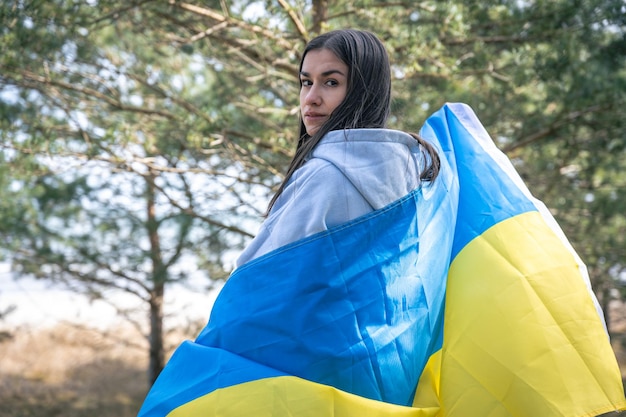 Een jonge vrouw gewikkeld in de vlag van Oekraïne op een onscherpe achtergrond