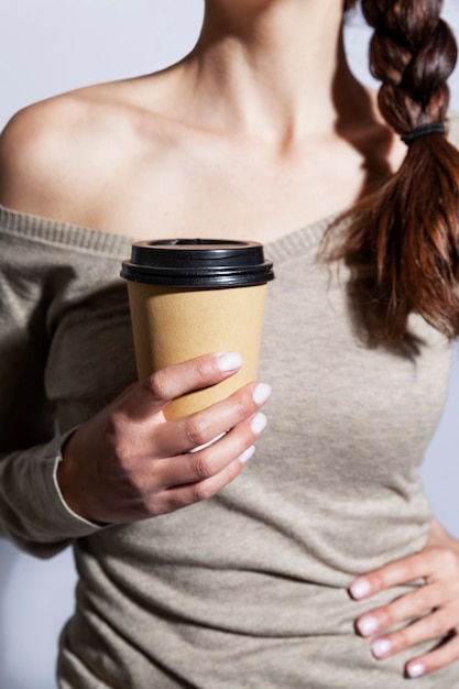 Een jonge vrouw houdt een ambachtelijke beker met koffie in haar hand. Verticaal.