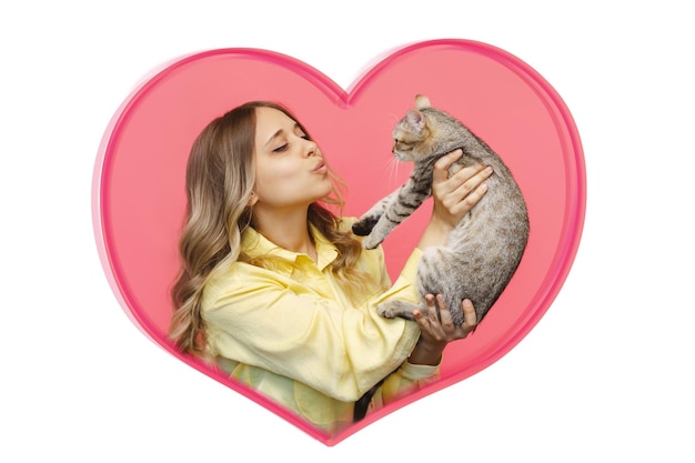 Een jonge vrouw houdt een kat in haar handen en bewondert hem in een hartvormig frame op een roze achtergrond