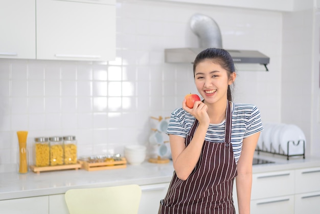 Een jonge vrouw houdt een rode appel vast in de keuken met een vrolijk gezicht