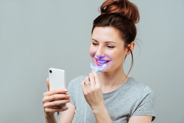 Een jonge vrouw houdt zich bezig met het bleken van tanden thuis voor het bleken van tanden met een uv-lamp