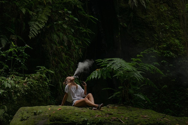 Een jonge vrouw in de jungle blaast rookwolken uit Vape