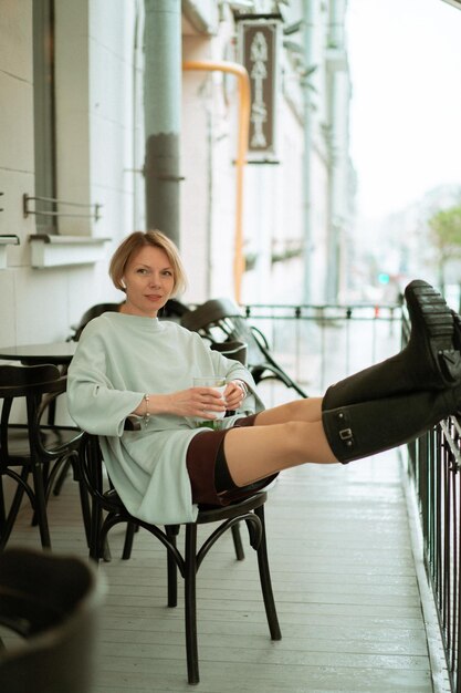 Een jonge vrouw in de regen op een open terras drinkt thee uit een groot glas