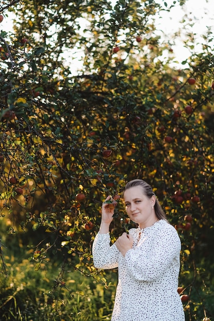 Een jonge vrouw in de tuin bij een appelboom die naar de camera kijkt