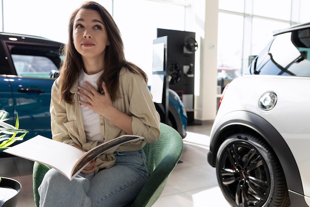 Een jonge vrouw in een autodealer bestudeert een catalogus met een complete set nieuwe auto's