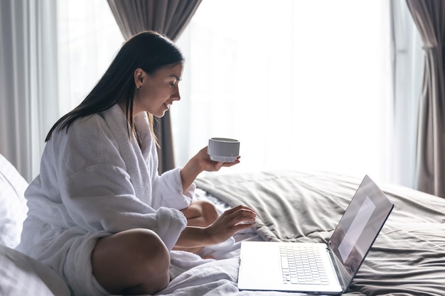 Een jonge vrouw in een badjas werkt op een laptop in bed