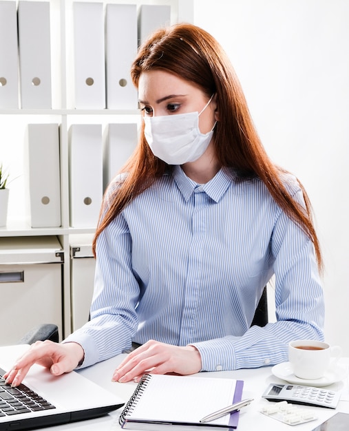 Een jonge vrouw in een beschermend masker werkt op een computer. zakenvrouw in een medisch masker op kantoor.