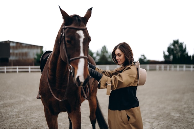 Een jonge vrouw in een bruine jas en hoed in de buurt van een paard foto van hoge kwaliteit