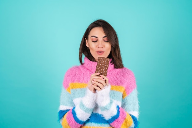 Een jonge vrouw in een felgekleurde trui op blauw geniet van elk stukje van een heerlijke reep luchtige melkchocolade