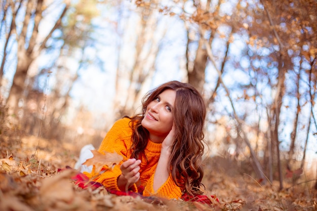 Een jonge vrouw in een herfstpark in een oranje trui