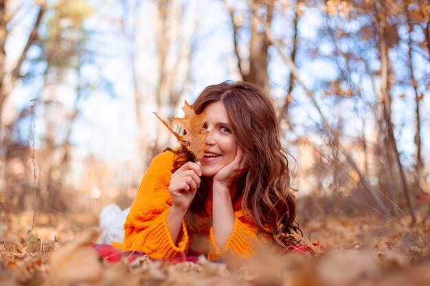 Een jonge vrouw in een herfstpark in een oranje trui