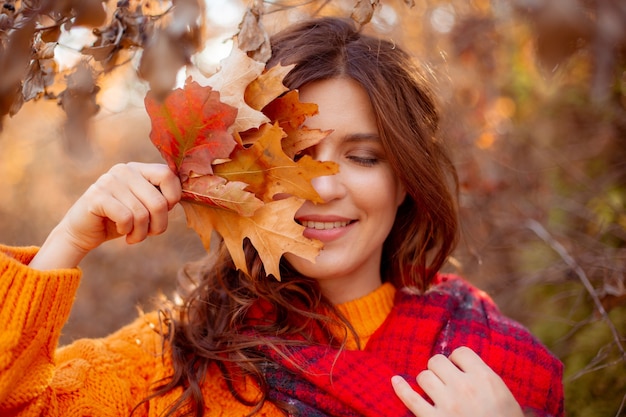 Een jonge vrouw in een herfstpark in een oranje trui