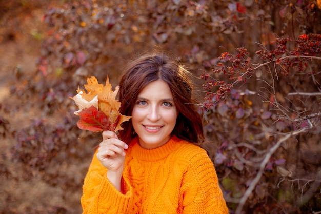 Een jonge vrouw in een herfstpark in een oranje trui