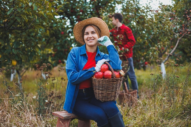 Een jonge vrouw in een hoed oogst sappige rode appels Een vrouw houdt een vliezen mandje met appels in de appelboomgaard