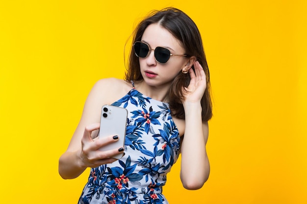 Een jonge vrouw in een jurk en een zonnebril typt op haar telefoon Studio modeportret