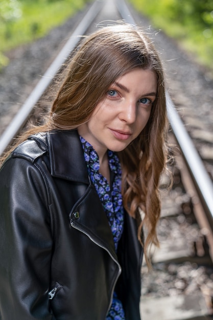 Een jonge vrouw in een lichtblauwe jurk en een zwart leren jack ging op de rails zitten