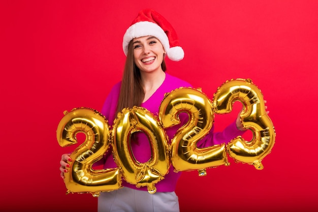 Een jonge vrouw in een lichte trui met een kerstmanhoed De brunette houdt de cijfers van het nieuwe jaar 2023 vast