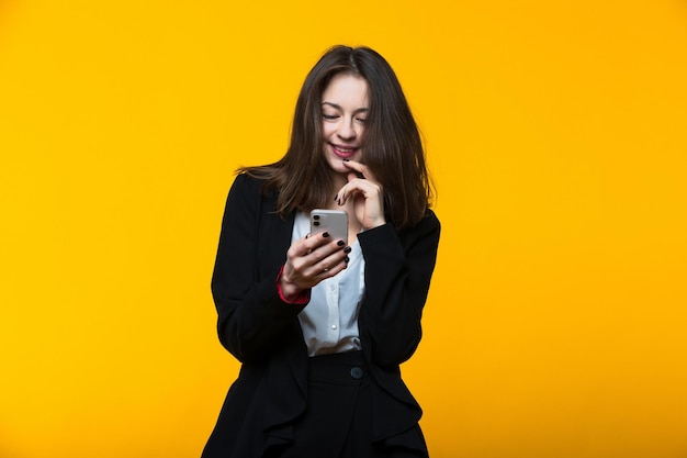 Een jonge vrouw in een pak typt op haar telefoon op een gele achtergrond