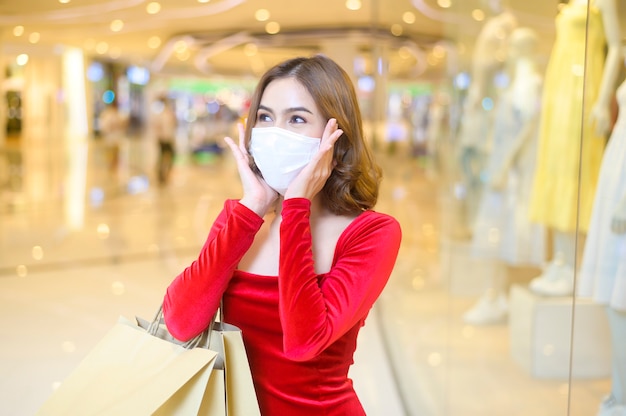 Een jonge vrouw in een rode jurk met een beschermend masker in een winkelcentrum, winkelend onder het pandemische concept van covid-19.