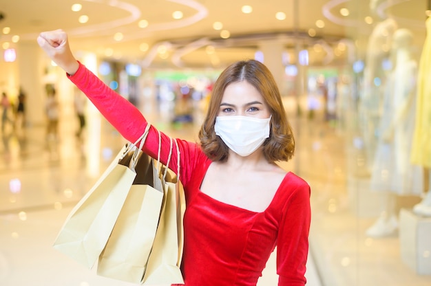 Een jonge vrouw in een rode jurk met een beschermend masker in een winkelcentrum, winkelend onder het pandemische concept van Covid-19.