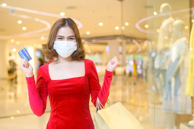 Een jonge vrouw in een rode jurk met een beschermend masker in een winkelcentrum, winkelend onder het pandemische concept van Covid-19.