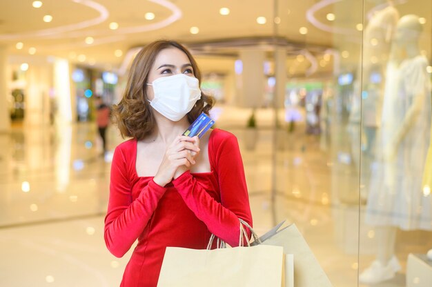 Een jonge vrouw in een rode jurk met een beschermend masker in een winkelcentrum, winkelend onder het pandemische concept van covid-19.