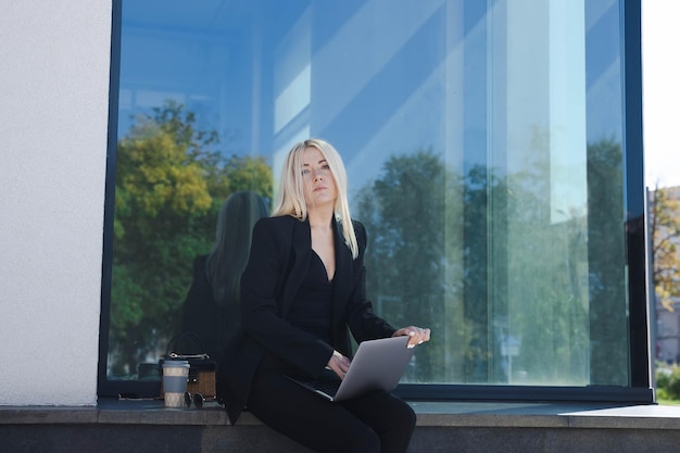 Een jonge vrouw in een stijlvol pak zit buiten en werkt op een laptop